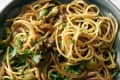 Spaghetti with olives, caramelized onions, and fresh parsley in a gray bowl.