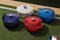 Four Le Creuset Dutch ovens in red, blue, white, and navy on grass, featuring MLB team logos.