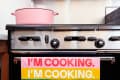 Pink pot on stove with colorful towel reading "I'm Cooking" in bold letters.