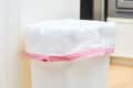White trash can with a pink-tinted liner in a kitchen setting.