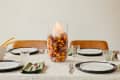 Dining table set with white plates, green napkins, and a centerpiece of nuts and berries in a glass vase with a candle.