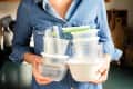 Person in denim shirt holding a stack of plastic food containers in a kitchen.