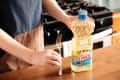 Someone holding fork upright next to bottle of vegetable oil.