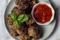 15 small meatballs sitting on a gray round plate with red sauce in a small round bowl on the plate, with three basil leafs on top