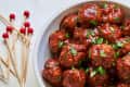 BBQ meatballs in a white bowl with toothpicks next to the bowl.