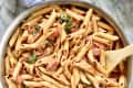 Tuscan chicken pasta made with penne pasta in a bowl with a wooden spoon.