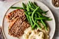 Meatloaf slices with green beans and mashed potatoes on a white plate.