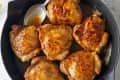 Golden-brown chicken thighs in a cast iron skillet with a spoon.