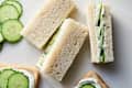 Cucumber sandwiches with cream cheese filling, sliced cucumbers, and white bread on a light surface.