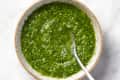 green chimichurri sauce in a bowl with a spoon in it on a marble surface
