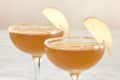 Two coupe glasses with harvest cocktail, cinnamon sugar rim and apple garnishes.