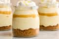 Head on shot of 3 small glass jars of creamy lemon mousse with layers of graham cracker crumbs and whipped cream, and topped with lemon zest.