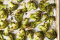 Overhead shot of roasted broccoli on white parchment paper, in a sheet pan.