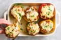 six stuffed peppers in baking dish; one being pulled