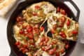 Chicken breasts topped with melted cheese, cherry tomatoes, and herbs in a skillet.