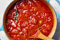 overhead shot marinara in a large pot with a wooden spoon in it