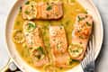 overhead shot of four pieces of lemon butter salmon in a skillet, topped with herbs and lemon