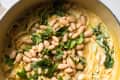 Creamy pasta with white beans and fresh spinach in a pot.
