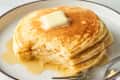Fluffy pancakes stacked on a plate, topped with a pat of butter and drizzled with syrup.