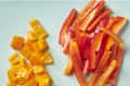 Overhead view of on cored yellow bell pepper, one cubed orange bell pepper and one red bell pepper cut into strips.