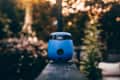 Blue portable device on a railing in a garden setting with blurred foliage.