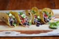 Black bean tacos with avocado, cabbage, and salsa on a wooden board, garnished with lime wedges.