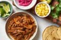Taco ingredients including pulled pork, pickled onions, lime wedges, pineapple, avocado, radishes, and cilantro.