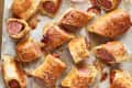 Pigs in a blanket on a baking sheet with bowls of ketchup and mustard.