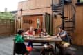 Family dining on a wooden deck with spiral staircase and open patio doors.