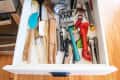 Open kitchen drawer with assorted utensils, including spatulas, wooden spoons, a whisk, and a bottle opener.