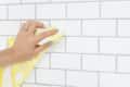 Hand cleaning white subway tiles with a yellow lemon-patterned cloth.