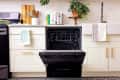 Open dishwasher in a modern kitchen with white cabinets, gold handles, a farmhouse sink, and a plant on the counter.