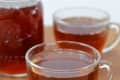 Two glass mugs and a jar filled with amber-colored tea on a wooden surface.