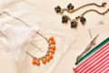 Two statement necklaces, one with orange beads and another with black and yellow stones, next to a striped pouch.