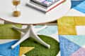 White round table with books and hourglass on a colorful geometric rug.