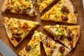 Breakfast pizza sliced into wedges, topped with scrambled eggs, sausage, and green onions on a wooden board.