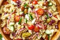 Pasta salad with cherry tomatoes, chopped cucumbers, red onions, olives, and other ingredients in a wooden bowl