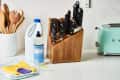 Wooden knife block with assorted knives, cleaning supplies, wooden utensils, and a mint green toaster on a kitchen counter.