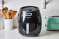 Cozyna air fryer on a kitchen counter with wooden utensils and a green toaster.