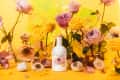 Brightland olive oil bottle surrounded by pink and yellow roses, garlic, and decorative vases on a vibrant yellow background.