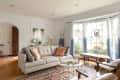 Cozy living room with a gray sofa, patterned rug, large windows, and wooden furniture.