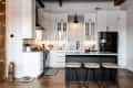 Modern kitchen with white cabinets, black fridge, marble island, and three wooden stools on a hardwood floor.