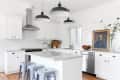 A bright white kitchen with large pendant light fixtures and a portrait in a gold frame on the counter