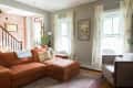 Living room with a rust-colored sectional sofa, patterned rug, potted plants, and framed art on a brick wall.