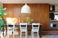 Dining area with wooden cabinets, black table, white chairs, wicker pendant light, and a potted plant.