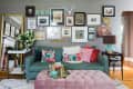 Living room with teal sofa, colorful pillows, pink ottoman, gallery wall, and decorative items on side tables.