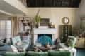 Living room with eclectic decor, featuring a fireplace, green sofa, patterned chairs, deer artwork, and various plants.