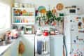 Colorful kitchen with open shelves, vintage decor, red kettle, potted plant, and fridge covered in magnets and notes.