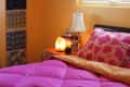 Cozy bedroom with pink bedding, a salt lamp on the nightstand, and a window with woven blinds.