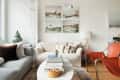 Modern living room with gray and cream sofas, orange chair, marble coffee table, and wall art above.